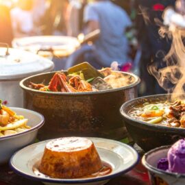 Traditionelle philippinische Gerichte auf einem Street-Food-Markt: dampfendes Kare-Kare im Tontopf, Sinigang mit Garnelen und Zitronengras, Sizzling Pork, cremiger Leche Flan und leuchtend violettes Ube-Eis authentisch und einladend präsentiert.
